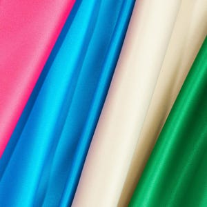 May include: Close-up of four fabric swatches in different colours: pink, blue, cream, and green. The fabric is smooth and silky.