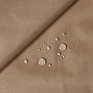 Pode incluir: Close-up de um tecido castanho com gotas de água na superfície. O tecido tem uma textura subtil e parece ser resistente à água.