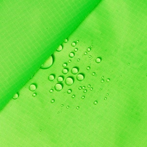 Può includere: Primo piano di una superficie di tessuto verde con goccioline d'acqua sparse. Le goccioline sono di dimensioni diverse e sembrano brillare alla luce.