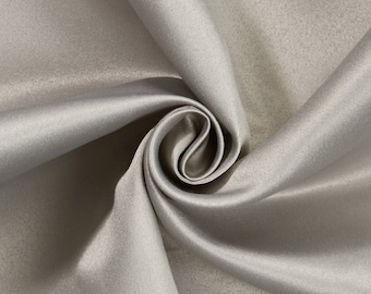 May include: Close-up of a swirl of light gray satin fabric. The fabric has a smooth, lustrous surface with subtle variations in tone, creating a soft, flowing appearance. The folds and curves of the fabric create a sense of depth and texture.