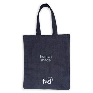 May include: A navy blue tote bag with the words "human made" printed in white. The bag also features the logo "fwd" in white. The bag has two handles and is made of a sturdy fabric.