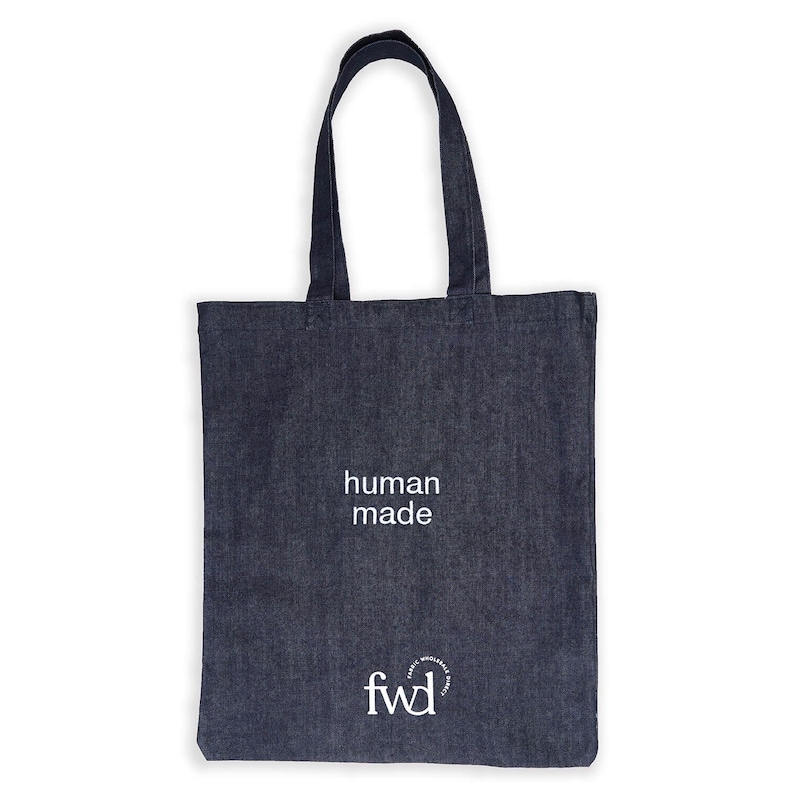 May include: A navy blue tote bag with the words "human made" printed in white. The bag also features the logo "fwd" in white. The bag has two handles and is made of a sturdy fabric.