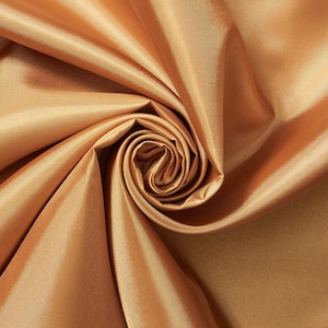 May include: Close-up of a golden-colored fabric with a satin finish. The fabric is artfully draped and swirled, creating a spiral pattern in the center. The folds and shadows highlight the smooth texture and sheen of the material. Ideal for apparel or home decor.