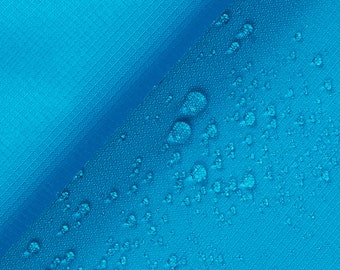 May include: Close-up of a blue fabric with water droplets on the surface. The fabric is folded in half, creating a diagonal line across the image.