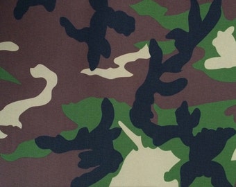 May include: Camouflage fabric with a brown, green, and black pattern. The fabric is measured with a ruler in inches.