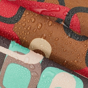 Pode incluir: Close-up de tecido estampado com gotas de água. O tecido apresenta um design retrô com formas marrons, vermelhas, pretas e turquesas. As gotas adicionam uma aparência texturizada e molhada ao material, destacando as cores e padrões.