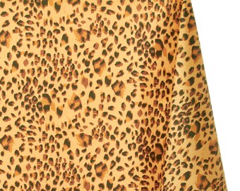 May include: A folded piece of fabric with a leopard print pattern. The fabric has a tan background with dark brown and black spots. The pattern is a classic animal print design.