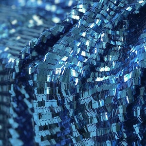 Puede incluir: Primer plano de una tela azul con lentejuelas. Las lentejuelas están dispuestas en filas y crean un efecto brillante.