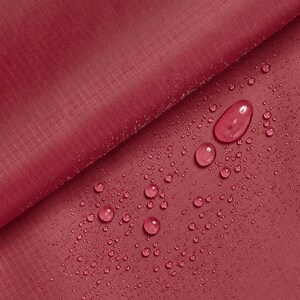 Può includere: Primo piano di un tessuto color borgogna con gocce d'acqua sulla superficie. Il tessuto è liscio e ha una lucentezza sottile.