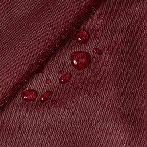 Könnte beinhalten: Nahaufnahme eines burgunderfarbenen Stoffes mit Wassertropfen auf der Oberfläche. Der Stoff hat eine subtile Textur und scheint wasserabweisend zu sein.