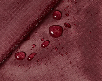 Puede incluir: Primer plano de una tela color burdeos con gotas de agua en la superficie. La tela tiene una textura sutil y parece ser resistente al agua.