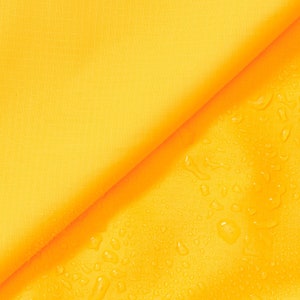 May include: A close-up of a yellow fabric with water droplets on the surface. The fabric is folded in half, creating a diagonal line.