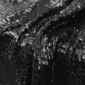 May include: Black fabric with a textured, sequin pattern. The sequins are small and closely spaced, creating a shimmering effect.