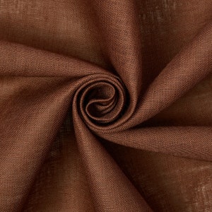 May include: Close-up of a brown linen fabric with a textured weave. The fabric is folded and twisted, creating a swirling pattern.