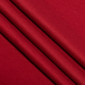 Könnte beinhalten: Nahaufnahme eines tief roten Stoffes mit einer strukturierten, gerippten Oberfläche. Der Stoff ist an mehreren Stellen gefaltet, wodurch weiche, abgerundete Falten entstehen.