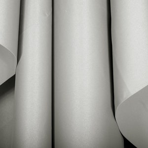 May include: Three rolls of white fabric are stacked on top of each other. The fabric has a subtle texture and a smooth, even surface.