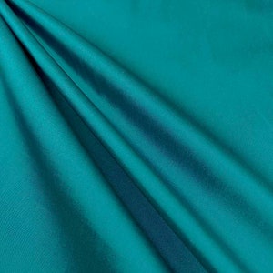 May include: A smooth, teal fabric with a soft, flowing drape. The fabric has a subtle sheen and a luxurious feel.