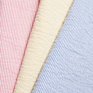 May include: A close-up of three sections of seersucker fabric in red and white stripes, yellow, and blue and white stripes. The fabric has a textured, puckered appearance, with vertical stripes. The colours are bright and vibrant, suitable for clothing or home decor.