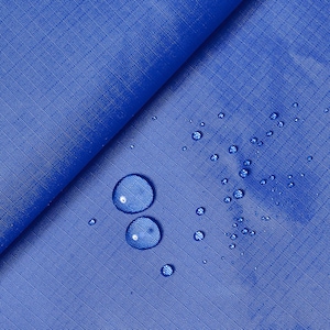Può includere: Primo piano di un tessuto blu con gocce d'acqua sulla superficie. Il tessuto è liscio e ha una leggera lucentezza. Le gocce d'acqua sono trasparenti e rotonde.
