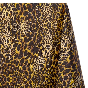 May include: A piece of fabric featuring a repeating leopard print pattern in shades of dark brown, black, and golden yellow. The material is draped to show the texture and the continuous nature of the animal-inspired spotted design.