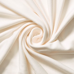 May include: A close-up shot of a cream-colored fabric, artfully arranged in swirling folds. The soft material creates a sense of depth and texture, with highlights and shadows emphasizing the curves. The fabric appears to be smooth and possibly a knit or jersey material.