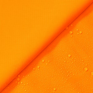 May include: A close-up of a bright orange fabric with a diagonal seam. The fabric is covered in small water droplets.