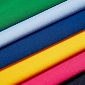 May include: A close-up shot of fabric swatches in a range of colours: green, pale blue, navy, yellow, and pink. The fabric has a textured finish and is arranged diagonally, displaying the colour variations.