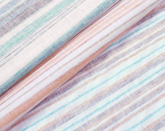 Può includere: Primo piano di tessuto piegato con motivo a righe. Il tessuto presenta strisce alternate bianche, azzurre, pesca e grigie. Il materiale sembra essere lino o un tessuto leggero simile, adatto per abbigliamento o arredamento.