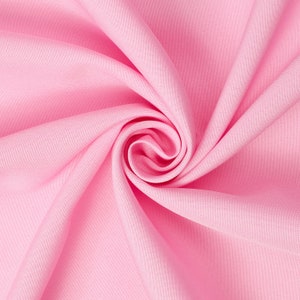 May include: A close-up of a soft, pink fabric with a smooth texture. The fabric is folded and draped in a way that creates a swirling pattern.