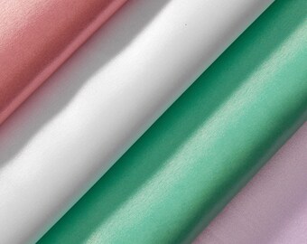 Puede incluir: Primer plano de cuatro rollos de tela en colores pastel. Los colores incluyen rosa, blanco, verde menta y lavanda. La tela tiene un ligero brillo, lo que sugiere un material de satén o seda. Los rollos están dispuestos en diagonal.