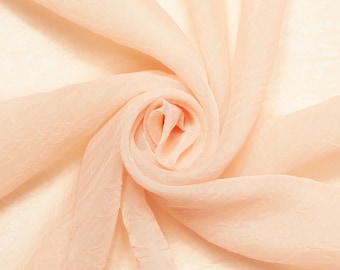 May include: A close-up of a peach-colored sheer fabric, draped and twisted into a spiral shape, creating a soft and delicate texture.