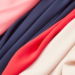 Könnte beinhalten: Nahaufnahme von Stoffmustern in verschiedenen Farben: Rosa, Marineblau, Rot und Off-White. Der Stoff wirkt glatt und fließend, mit sichtbaren Falten und Knitterstellen.