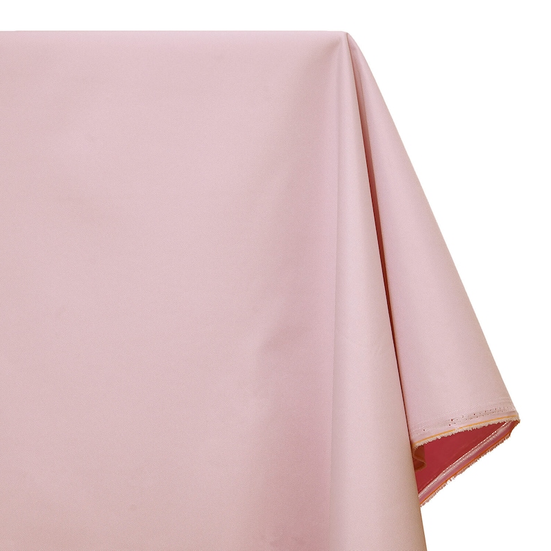Puede incluir: Un mantel de mesa de color rosa p&aacute;lido con una textura lisa y uniforme. El mantel est&aacute; doblado por la mitad y los bordes son visibles.