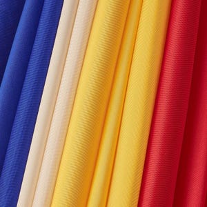 May include: Close-up of folded fabric in a variety of colors. The colors include blue, cream, yellow, and red. The fabric appears to be a solid color and has a slight sheen. The folds create a textured effect.