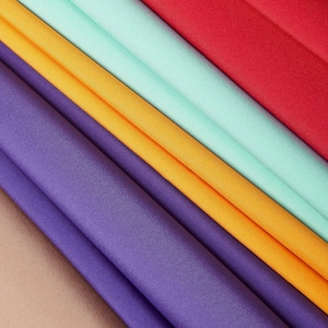 Könnte beinhalten: Abstrakte Darstellung von gefaltetem Stoff in verschiedenen Farben. Die Farben umfassen Rot, Mintgrün, Gelb, Lila und Beige. Der Stoff ist diagonal angeordnet und erzeugt einen geschichteten Effekt. Der Stoff scheint glatt zu sein, möglicherweise Seide oder Satin.