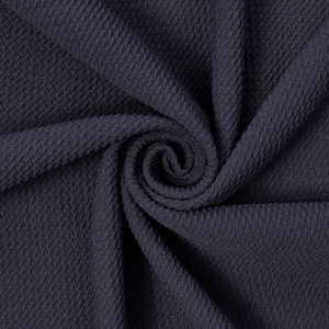 May include: A close-up shot of a navy blue fabric with a textured, woven pattern. The fabric is arranged in soft folds, with a spiral at the center. The material has a subtle sheen, and the weave creates a diagonal ribbed effect.