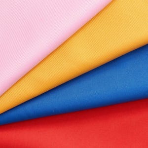 May include: A close-up of four fabric swatches in pink, gold, blue, and red. The fabric is folded diagonally, showcasing the different colors and textures. The colors are vibrant and saturated, creating a visually appealing display.