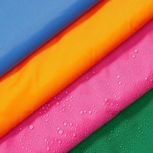 Puede incluir: Primer plano de cuatro muestras de tela coloridas: azul, naranja, rosa y verde. La muestra rosa tiene gotas de agua. Las telas están dispuestas en diagonal, creando una exhibición vibrante y texturizada.