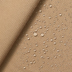Könnte beinhalten: Nahaufnahme eines beigefarbenen Stoffes mit Wassertropfen auf der Oberfläche. Der Stoff hat eine subtile Textur und scheint wasserabweisend zu sein.