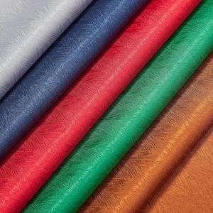 May include: A close-up of several rolls of fabric in various colours. The colours include silver, navy blue, red, green, and bronze. Each fabric has a textured, diagonal pattern. The rolls are arranged diagonally across the frame.
