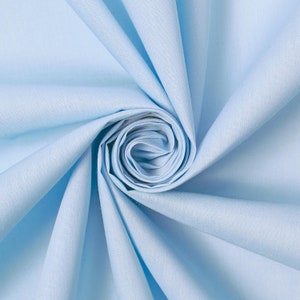 May include: A close-up of light blue fabric, arranged in a spiral. The fabric's texture is visible, with soft folds and shadows. The overall effect is one of gentle movement and a smooth surface. The fabric is likely cotton or linen.