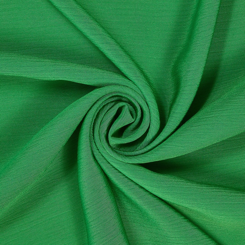 May include: A close-up of a green fabric with a soft, flowing texture. The fabric is folded and draped in a spiral pattern, creating a sense of movement and depth.