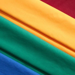 Peut inclure: Gros plan sur du tissu plié de différentes couleurs. Les couleurs comprennent le bleu, le vert, le jaune et le bordeaux. Le tissu semble être un matériau lisse et uni, peut-être du coton ou un textile similaire. Les plis créent des lignes diagonales.