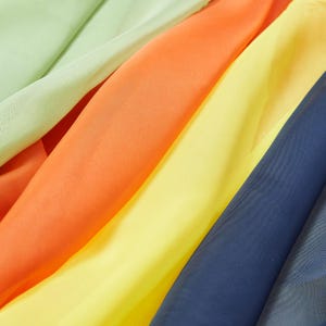 May include: A selection of colourful fabric swatches in shades of green, orange, yellow, and navy blue. The fabric appears lightweight and flowing, with a slight sheen. The colours are vibrant and saturated, creating a visually appealing display of textiles.