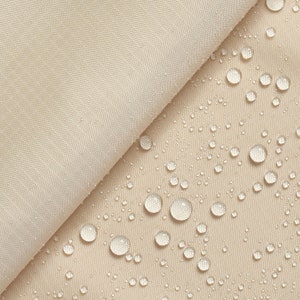 Può includere: Primo piano di un tessuto beige con gocce d'acqua sulla superficie. Il tessuto è liscio e ha una leggera lucentezza.