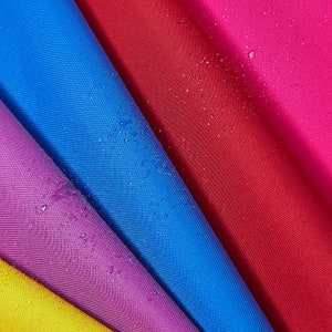 May include: Close-up of a colorful fabric with a water-resistant finish. The fabric is folded in a fan shape, revealing shades of yellow, purple, blue, red, and pink. Water droplets are visible on the surface of the fabric.