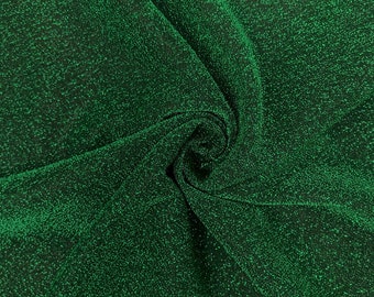 May include: Green sparkly fabric with a textured, glittery surface. The fabric is folded and twisted, showing the texture and sheen.