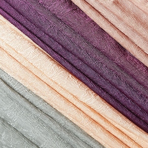 May include: A selection of textured fabric swatches in various colours. The fabrics include shades of purple, peach, and grey. The material has a crinkled appearance, creating a unique visual texture. The fabrics are arranged diagonally.
