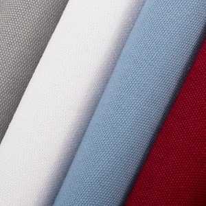May include: Close-up of four rolls of fabric in varying colors. The colors include gray, white, light blue, and red. The fabric has a textured weave, and the rolls are arranged diagonally across the frame.