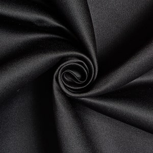 May include: A close-up of a swirl of black satin fabric. The fabric is smooth and shiny, with a slight sheen. The folds create a spiral pattern, highlighting the fabric's texture and depth. The overall effect is elegant and luxurious.